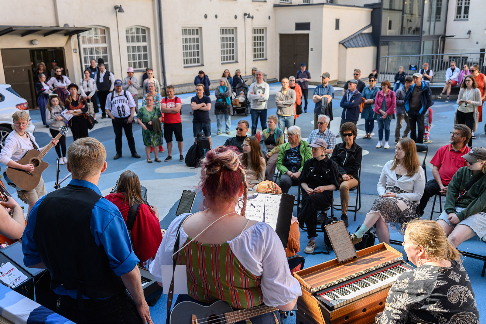 Kymmeniä ihmisiä kuuntelee ulkolavalla kesäisissä tunnelmissa musiikkiesitystä.