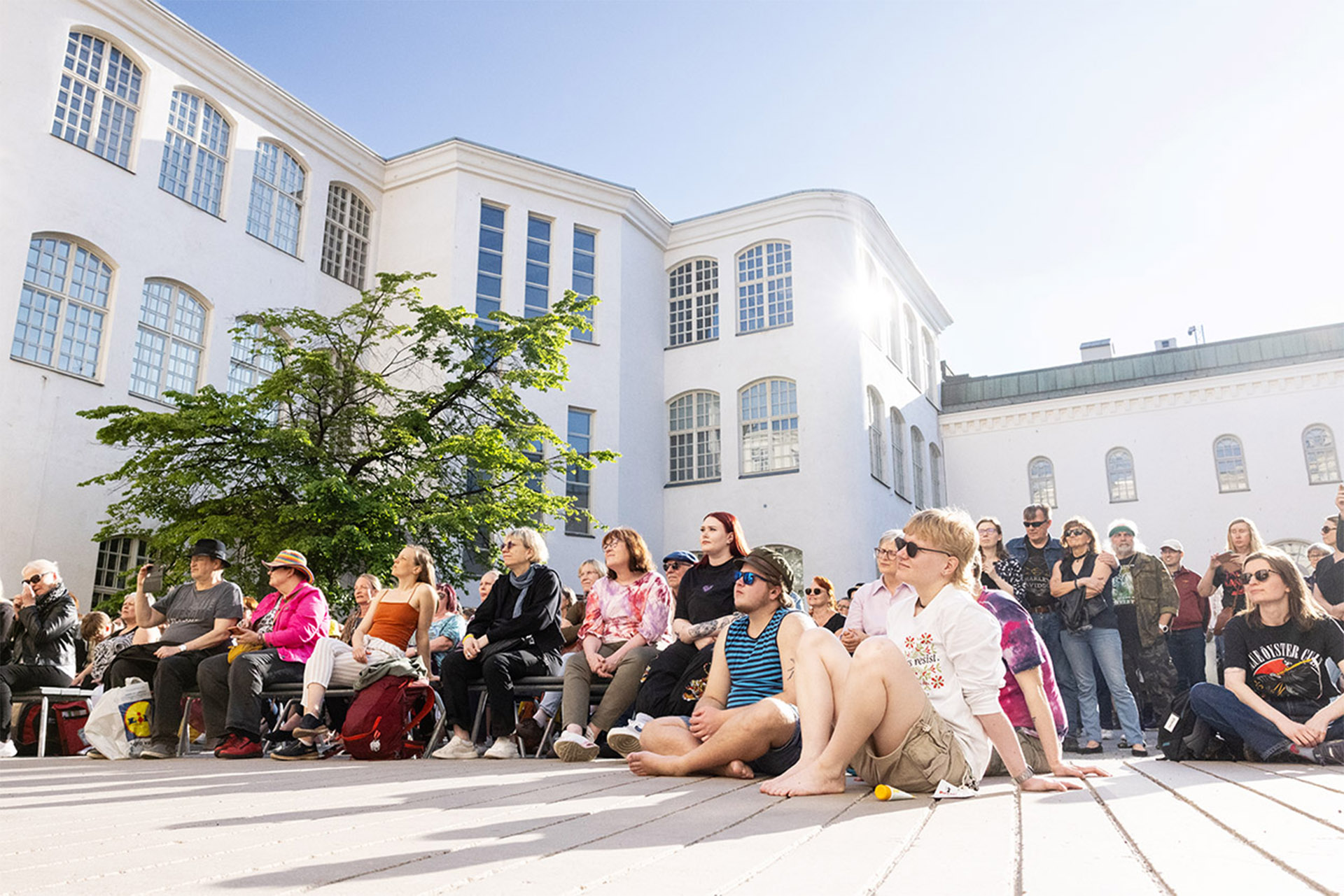 Yleisö nauttii konsertista aurinkoisessa säässä pelkeillä ja maassa istumalla.