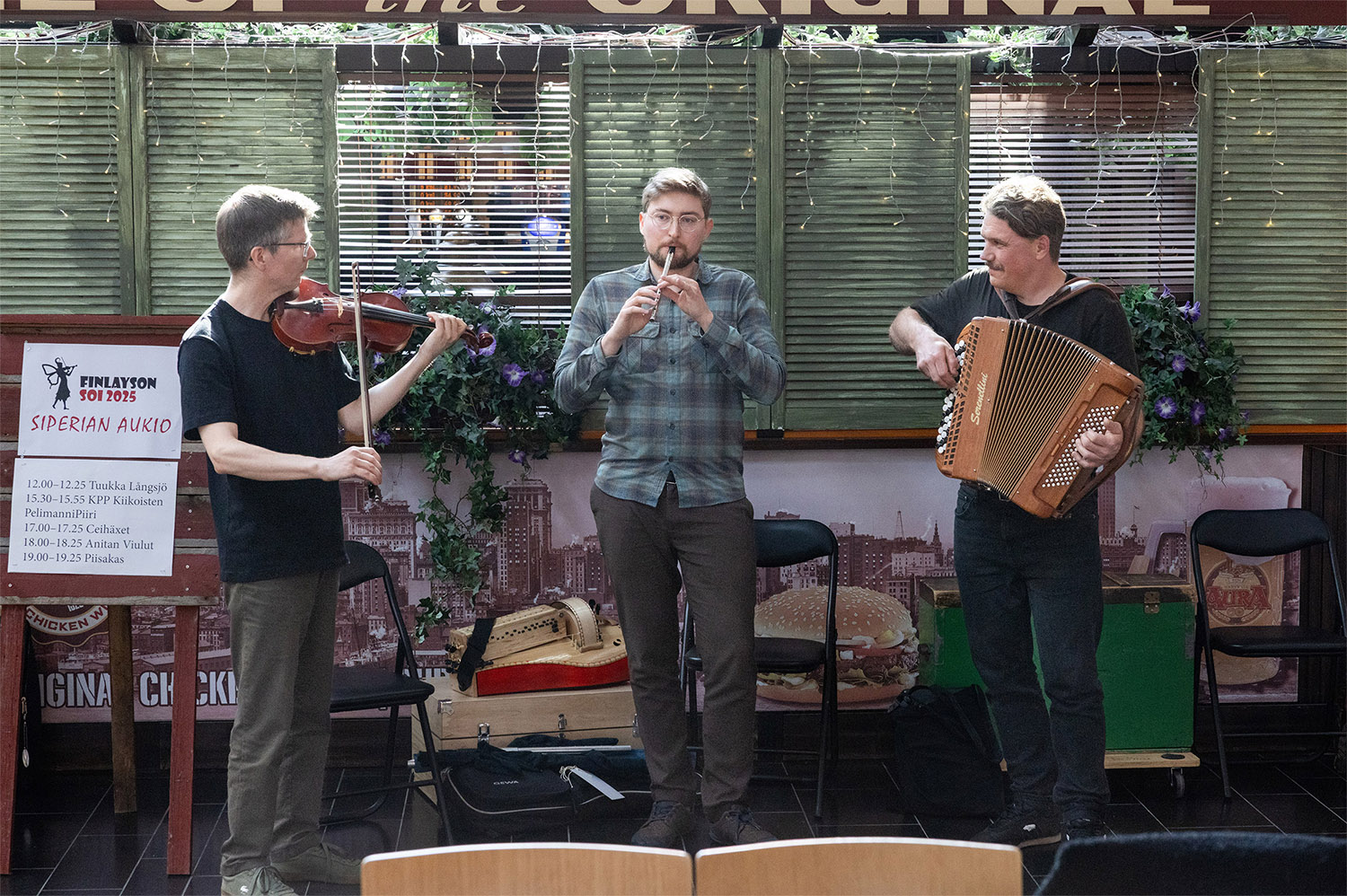 Kolmen miehen pelimanniyhtye soittaa sisäaukiolla.