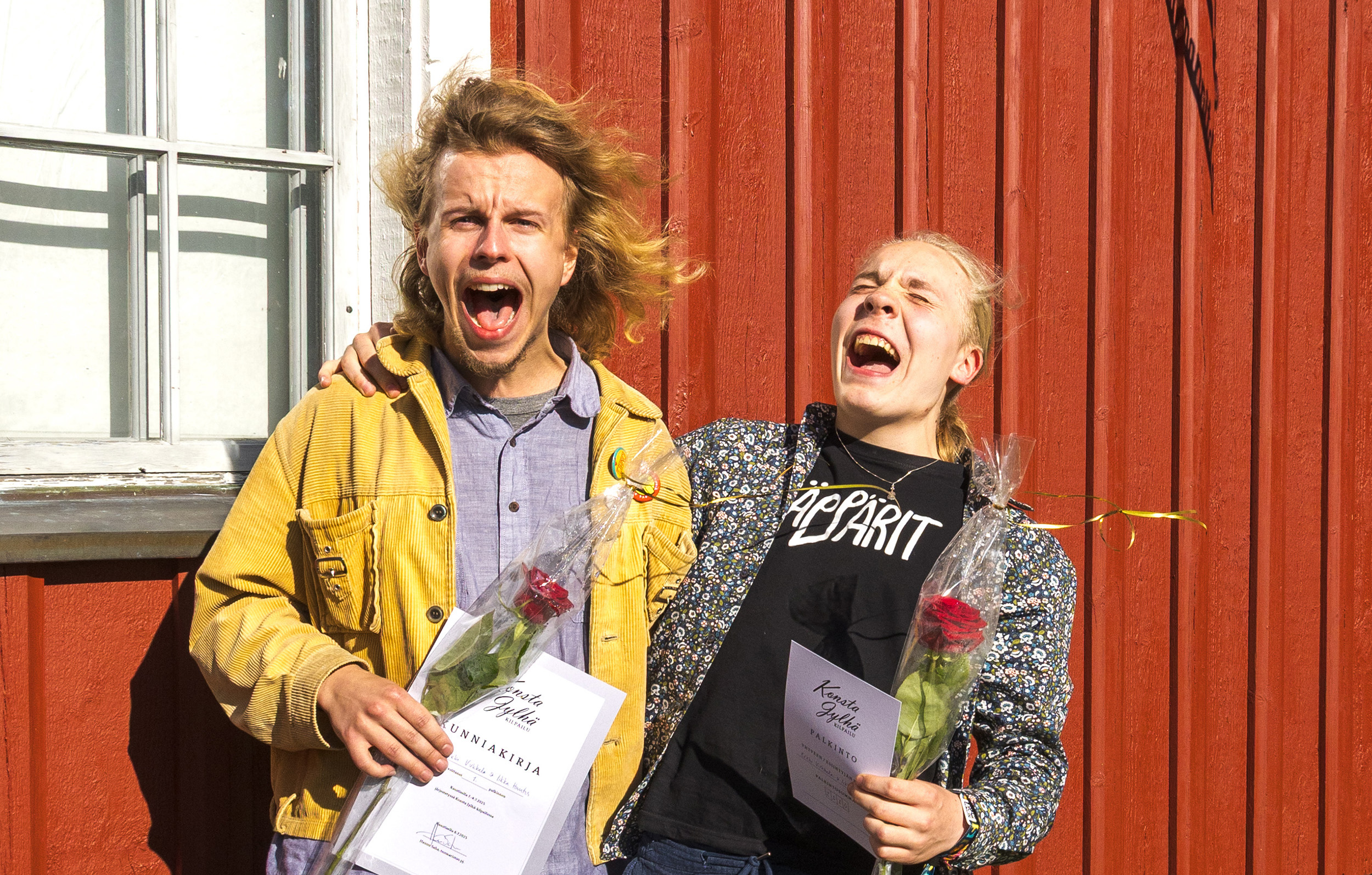 Kaksi nuorukaista ulvoo naurusta ulkona Kaustisen Pelimannitalon seinustalla.