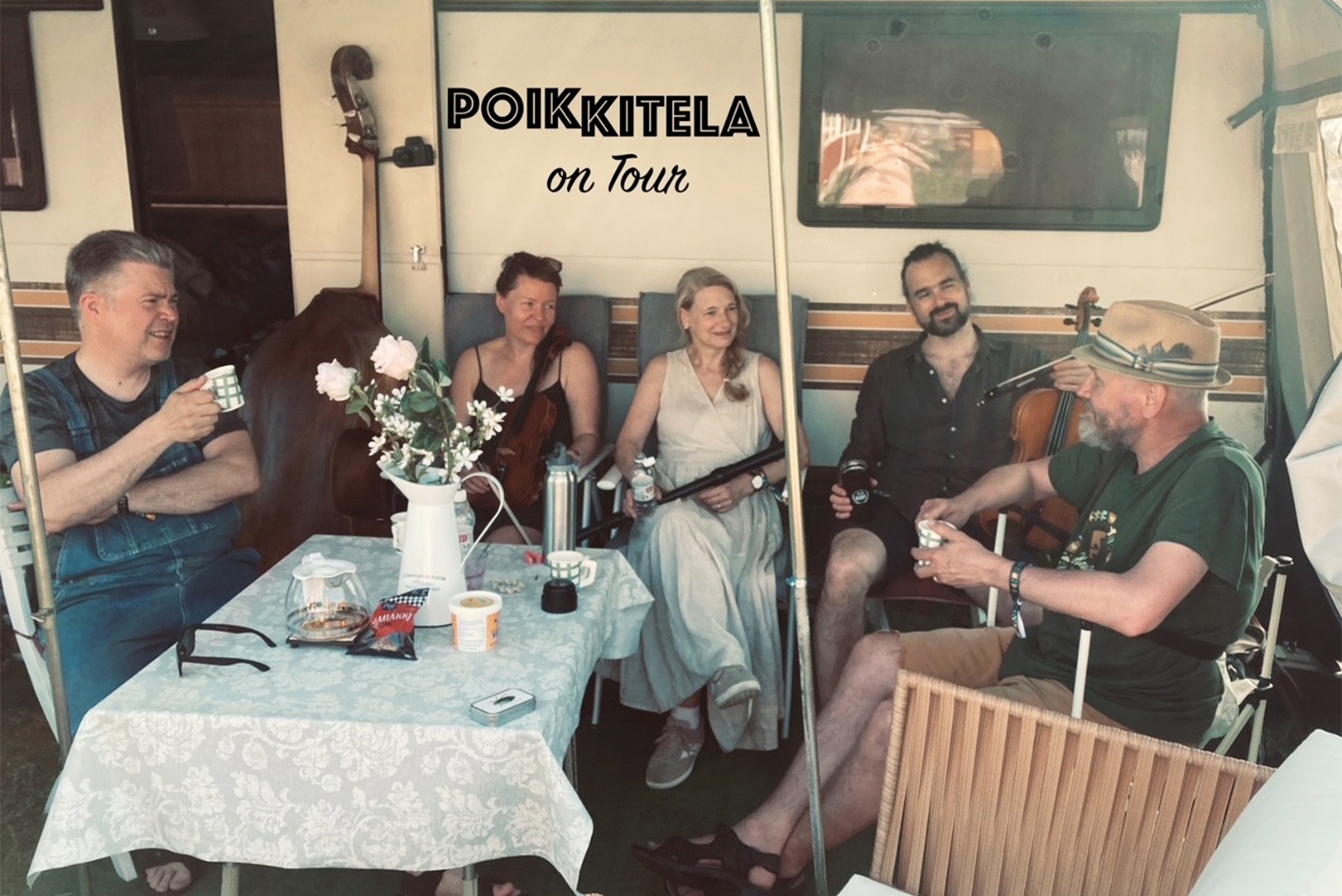Poikkitela_finlayson-soi Viisi muusikkoa istuskelee rennosti asuntovaunun edessä.