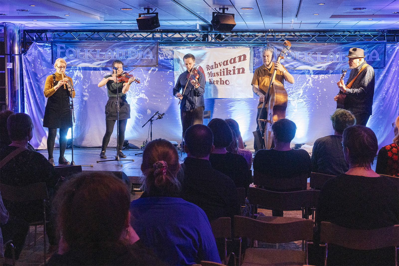 Yhtye keikalla, yleisöä istuu etualalla.